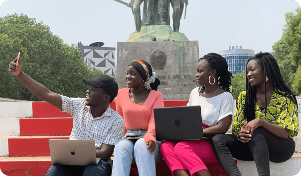 Four young Nigerians sitting on steps working on laptops outdoors