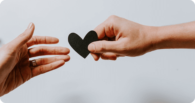 Two hands exchanging a paper heart, symbolising giving and compassion
