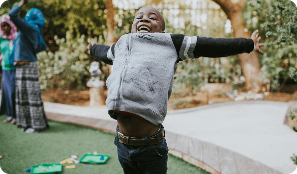 A joyful child with arms spread wide outdoors – Carry Them Ministries